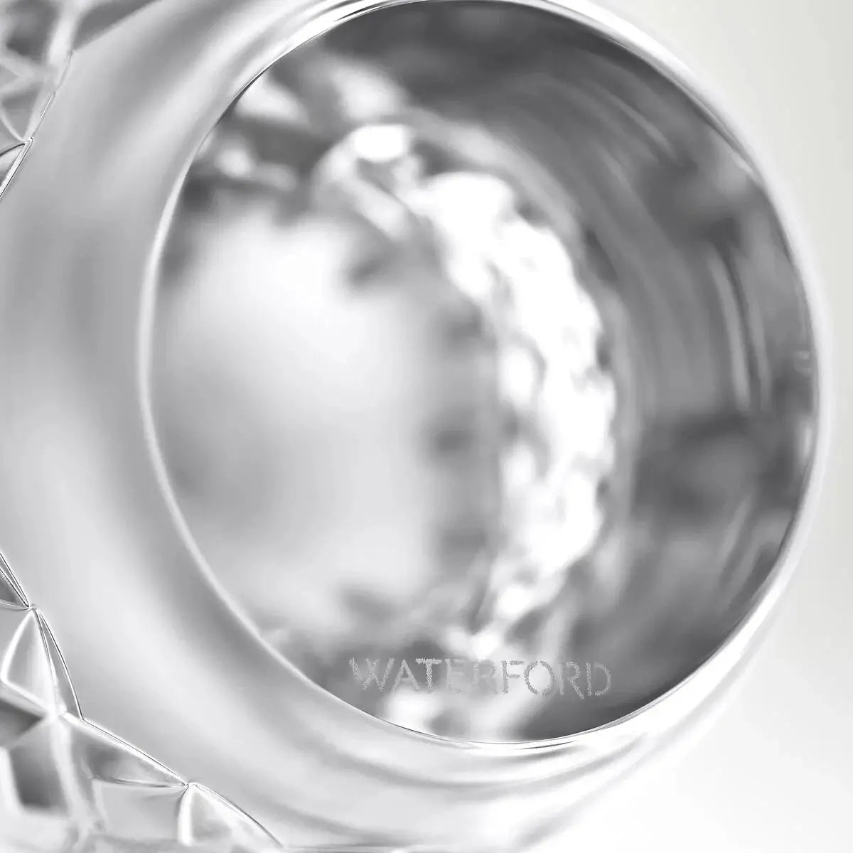 Close-up of a polished silver-toned cup or tumbler with a faceted cut-glass base, showing the engraved brand name WATERFORD near the rim.