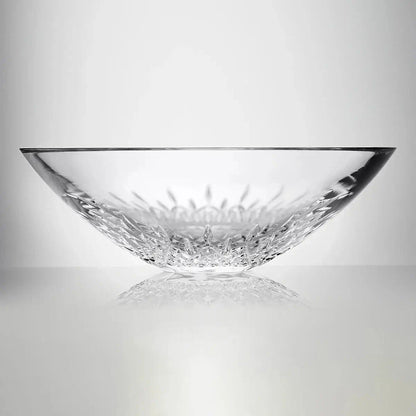 A clear cut-glass bowl with a textured, faceted base, photographed on a reflective light gray surface against a neutral gray background.