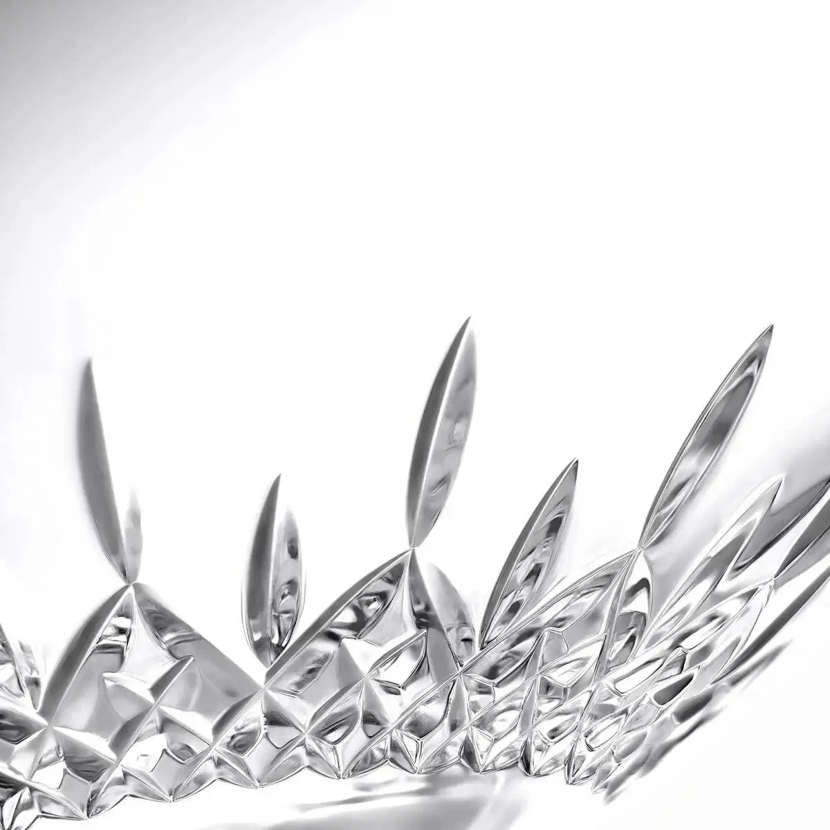 A close-up studio shot of a clear faceted glass object with sharp geometric cut patterns, photographed against a bright white background.