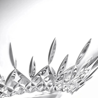 A close-up studio shot of a clear faceted glass object with sharp geometric cut patterns, photographed against a bright white background.