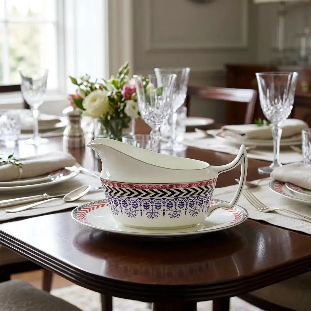 Decorative gravy boat on a table with a floral arrangement and glasses in a dining setting