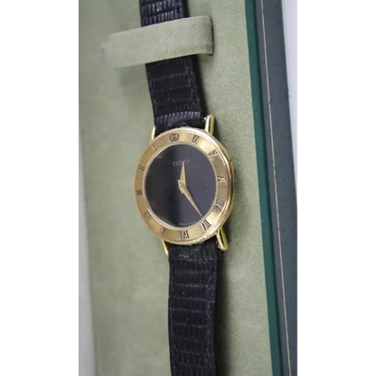 Gold watch with a black strap on a green cushion