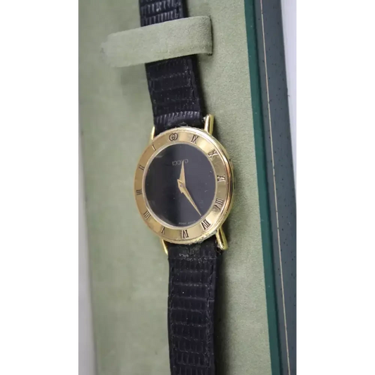 Gold watch with a black strap on a green cushion
