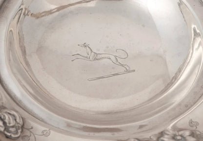 Close-up of the interior of a polished silver-toned bowl or plate, showing a engraved leaping dog motif near the center.