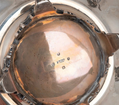 Close-up of the interior bottom of a polished silver-toned metal pot or vessel, showing a reflective interior surface with a small maker's mark and decorative edge details.