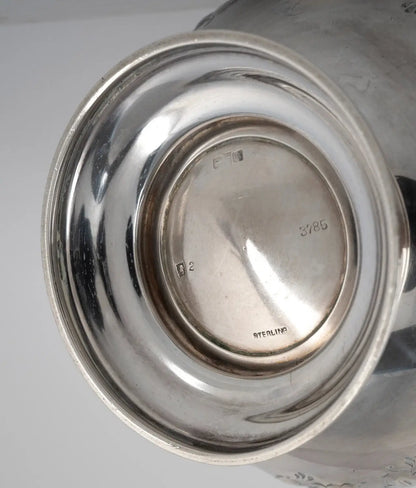 Close-up of the polished silver base of a metal vessel, showing engraved maker's marks and the word 'STERLING' on a light gray background.