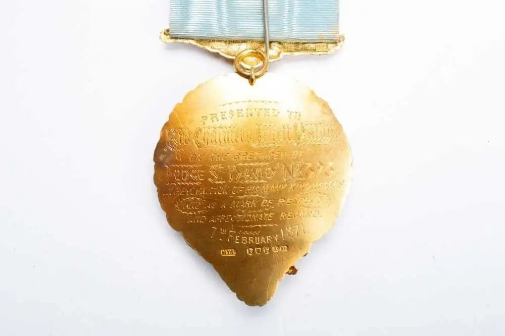 A gold-colored historical military medal pendant with engraved text, suspended from a light blue ribbon on a plain white background.