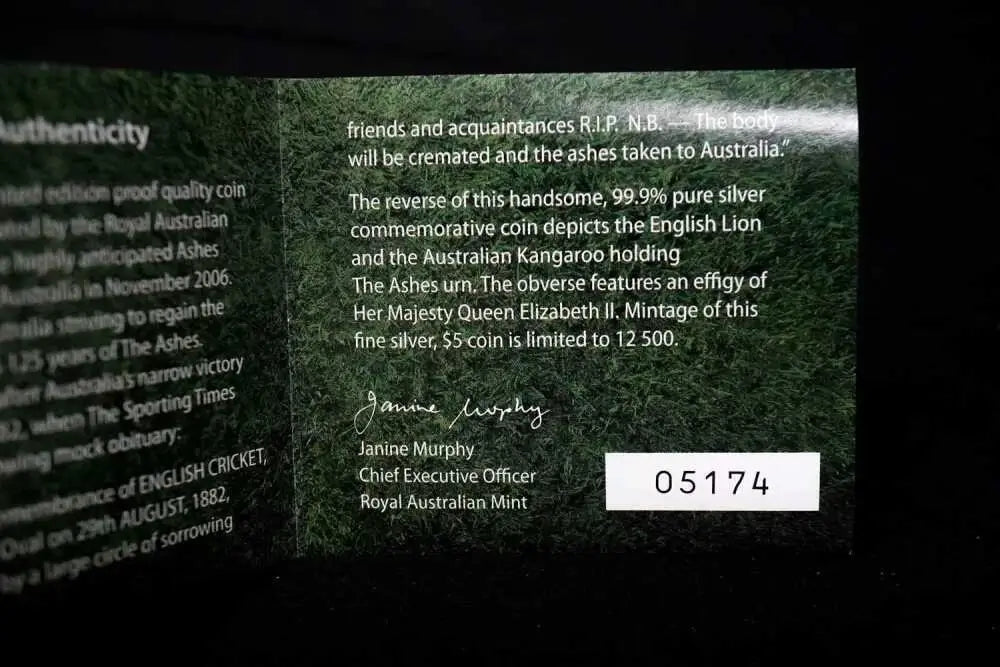 A close-up of a dark green Australian commemorative coin authenticity card with printed text, a signature, and a white label reading 05174 on a black background.