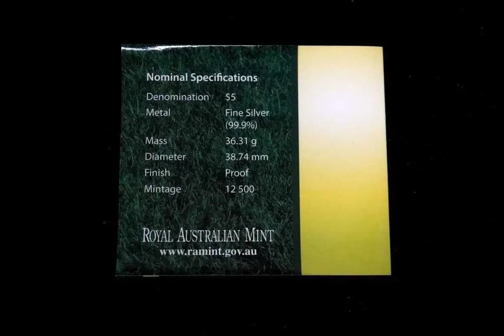 A small rectangular card from Royal Australian Mint showing nominal specifications for a $5 coin, with a dark green textured left side and a yellow-to-white gradient right side, photographed against a black background.