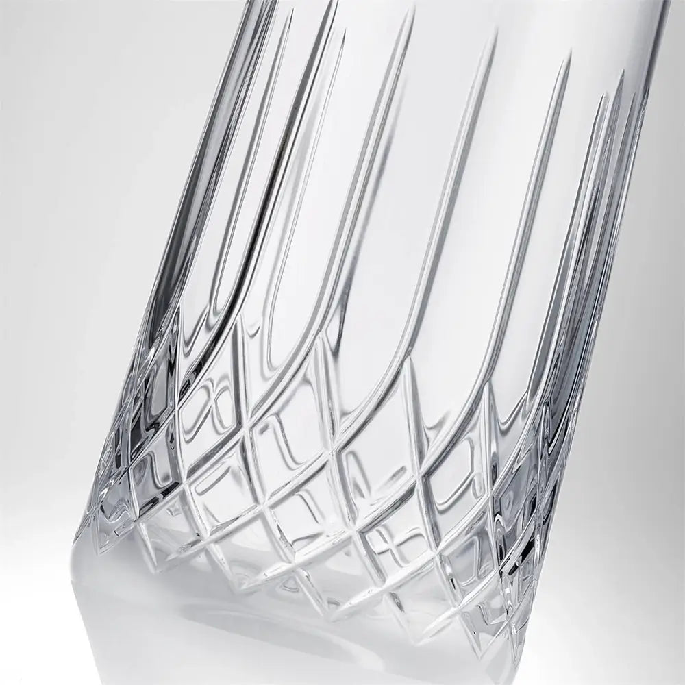 A close-up of a clear cut-crystal glass carafe with a geometric lattice pattern and vertical fluted sides, set against a light gray gradient background.
