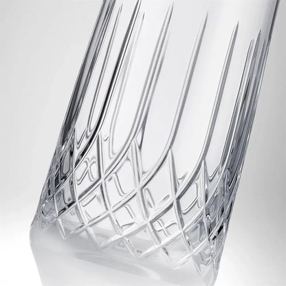 A close-up of a clear cut-crystal glass carafe with a geometric lattice pattern and vertical fluted sides, set against a light gray gradient background.