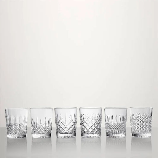Six clear cut-crystal tumblers with different diamond and geometric patterns, lined up in a row on a reflective white surface against a light gray background from our Waterford Crystal Australia – Outlet & Sale Collection