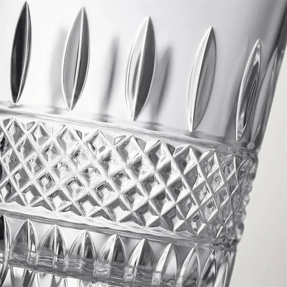 Close-up of a clear cut-glass tumbler showing reflective facets, a diamond pattern band, and leaf-shaped cutouts near the rim against a light gray background.