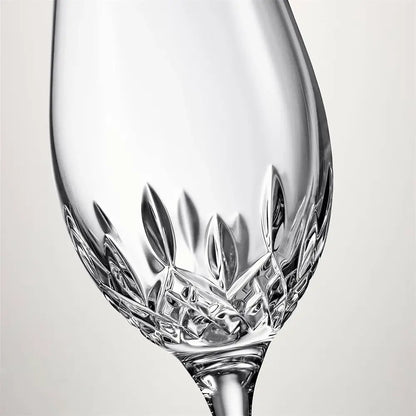 A close-up studio shot of a clear cut-crystal wine glass with a textured, geometric pattern around the base, set against a neutral light gray background.