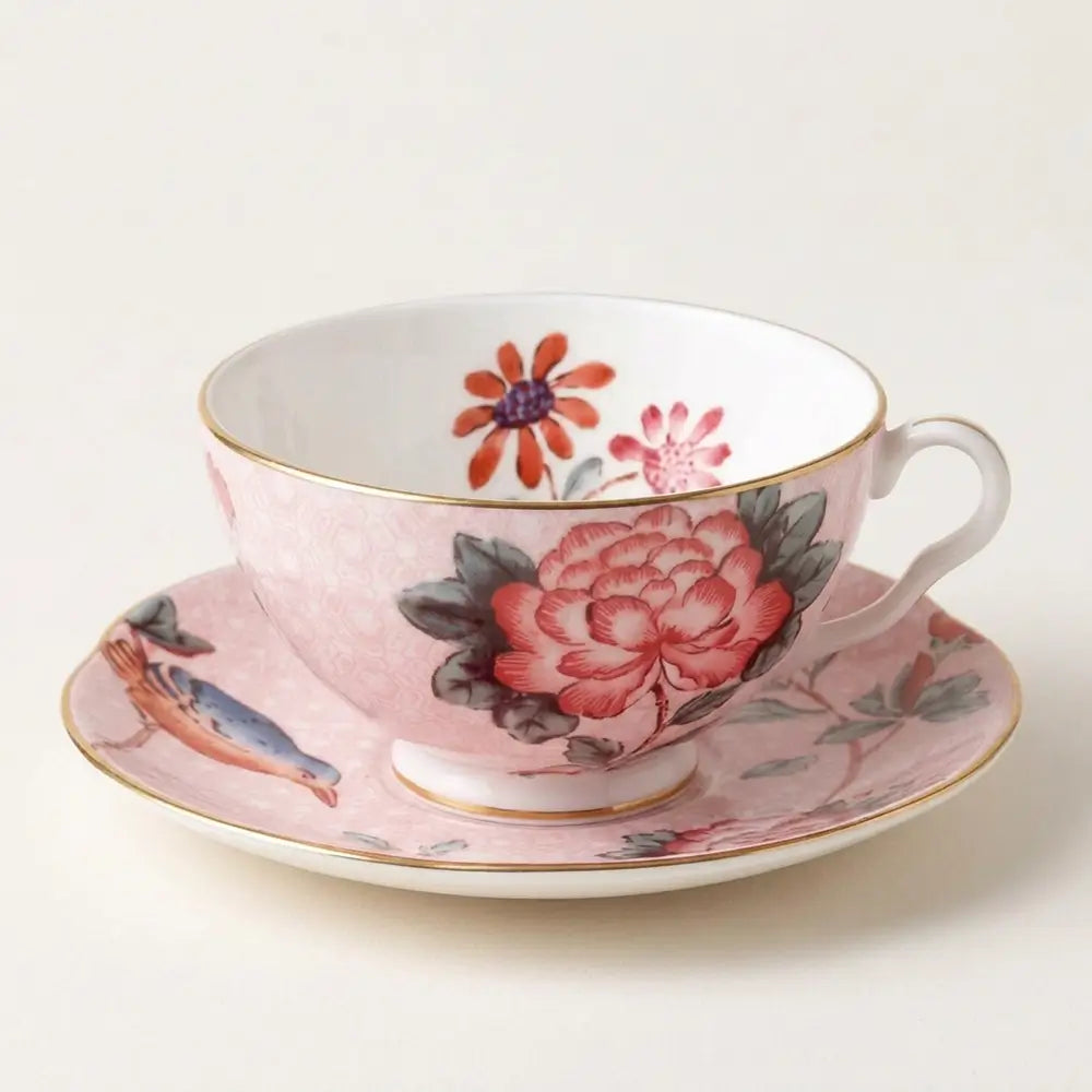 Professional studio photography of a Wedgwood Paeonia Blush teacup and saucer in soft pale pink, featuring detailed peony and bird motifs with a gold rim.
