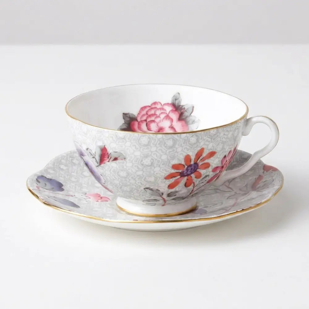 High-resolution e-commerce shot of a Wedgwood Paeonia Blush teacup and saucer in elegant grey, showcasing pink peony and orange floral patterns with a gold handle